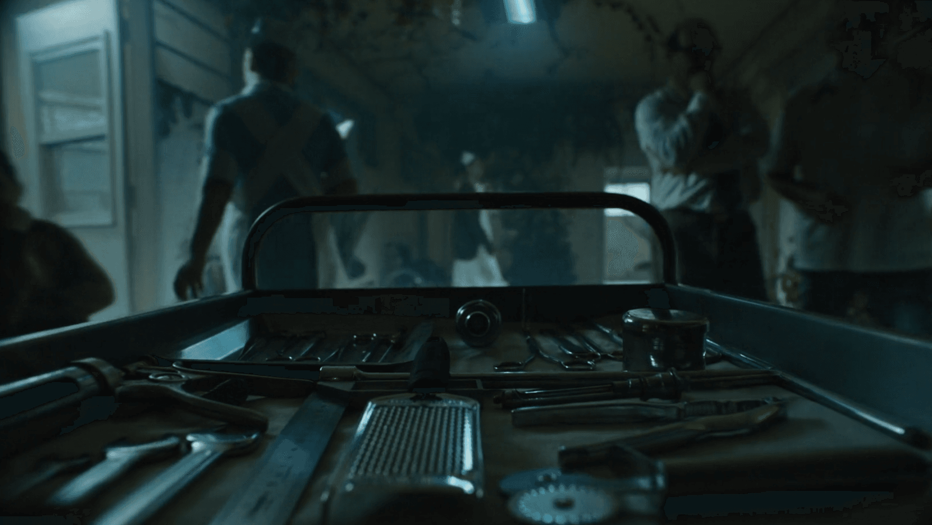 A dark, suspenseful scene looking across a tray of metal instruments